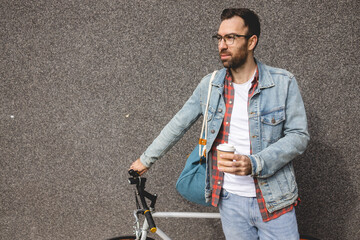 A young man leaning on a bicycle holds a cup of coffee