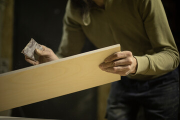 Carpenter grinds board. Man creates furniture. Hands hold sanding paper.