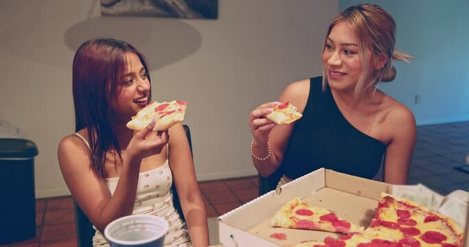 Two young women enjoy pepperoni pizza and laugh in their kitchen together