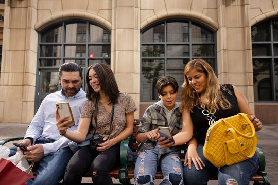 Tourist Family Using Smart Phones On Urban Bench