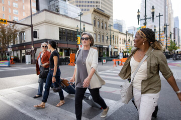 Mature women friends with suitcases crossing city street at crosswalk