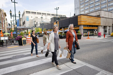 Mature women friends crossing city street with shopping bags