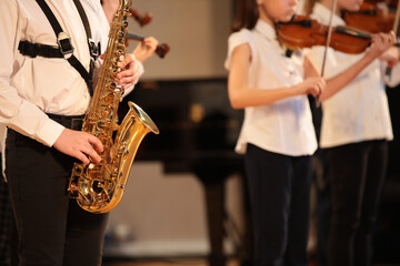 A group of children students young musicians boys and girls with musical instruments golden saxophone violin standing in a row playing together.The concept of school music education for young people