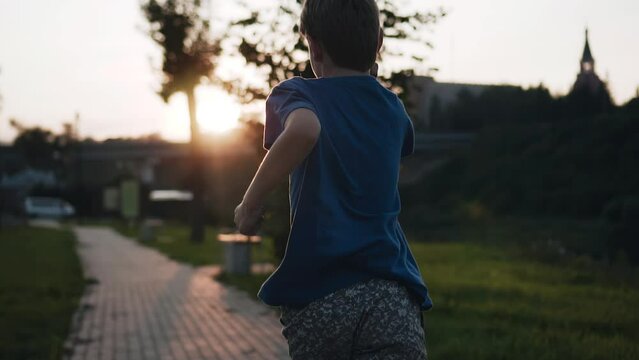 A boy runs along the embankment in the evening in the city enjoying the summer weather. Shooting from behind in slow motion