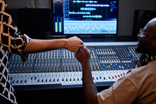 Professional African American music producer and young singer finishing work on album in recording studio doing fist bump