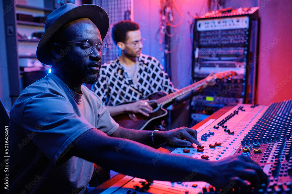 Poster selective focus shot of stylish mature african american producer adjusting sound on mixer while youn