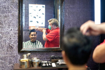 Mirror image of a barber cutting a customer's hair