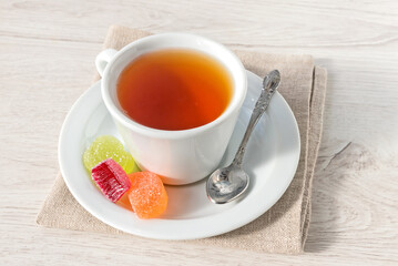 A cup of hot tea with jelly fruit marmalade on a linen napkin.