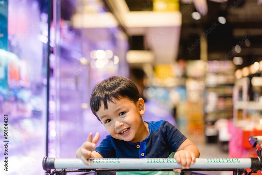 Wall mural toddler boy child sitting on shopping cart during family shopping on grocery store hypermarket.kid b