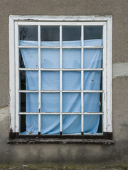 An old white wooden window with many square panes, covered with a blue sheet.