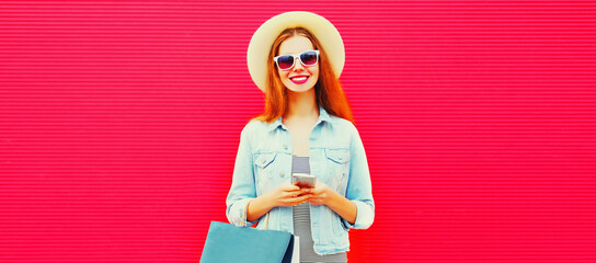 Portrait of beautiful young woman looking at smartphone with shopping bag wearing summer straw hat...