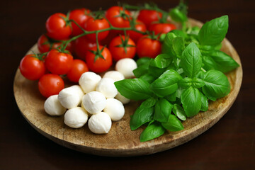 A set of products for caprese salad. Tomatoes, basil and mozzarella on a wooden board.