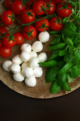 A set of products for caprese salad. Tomatoes, basil and mozzarella on a wooden board.