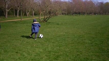 Happy Family Of Children Having Fun In Spring Park. Little Kid Run. Child Boy Dribbles Black White Classic Soccer Ball On Green Grass. People Playing Football. Childhood, Sport, Championship Concept