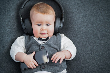 Cute little well dressed smart baby business man in vest and bow tie with big earplugs, headphones...