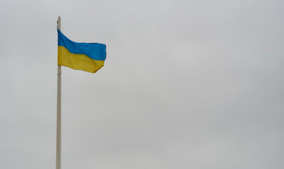 Ukrainian flag on white flagpole on gray sky