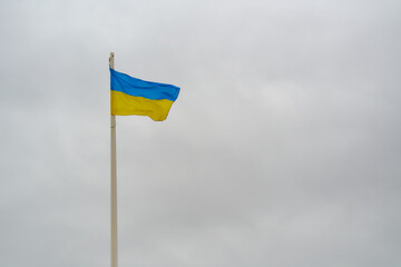 waving flag of ukraine on white flagpole over dark sky