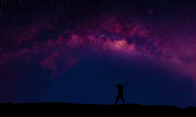 A person standing happily beside the Milky Way Galaxy pointing to a bright star.