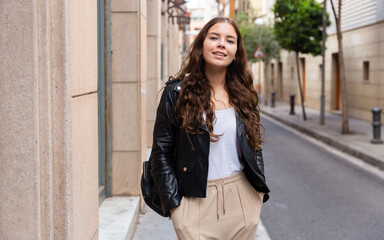 Obraz premium Elegant young woman wearing black leather jacket posing in time walking on the street of old city