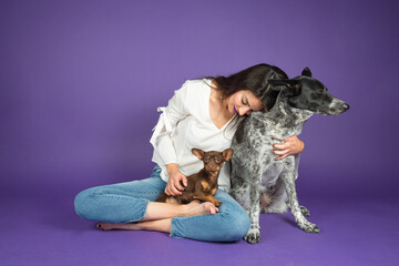 young latin woman hugs her chihuahua dog on a purple isolated background