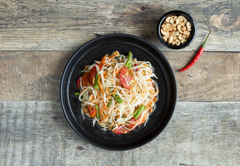 Traditional Thai papaya salad with roasted peanuts, tomatoes, Chinese beans on a wooden background,...