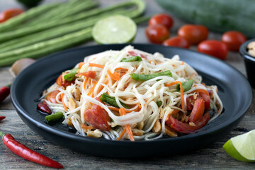 Bowl of papaya salad with ingredients on a wooden table, close up, side view. Traditional Thai food.