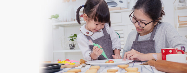 Portrait of little asian girl and mother baking cooking decorate cake and cookies in the kitchen....