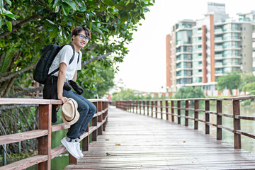 Happy man travel mangrove forest. Tourist traveler wear white shirt with hat for backpack activity. asian man ready to go hiking. Relax time on holiday concept travel.