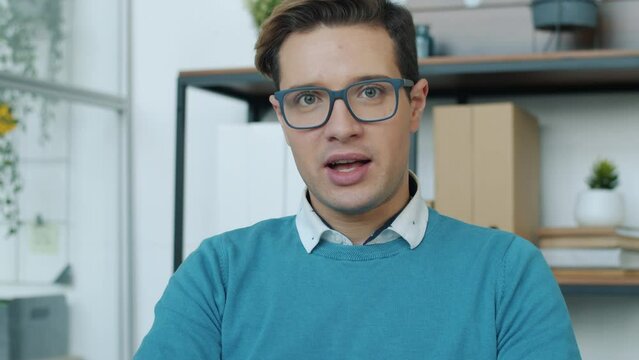 Joyful young businessman enjoying vitual meeting speaking and laughing looking at camera in office. Job and communication concept.