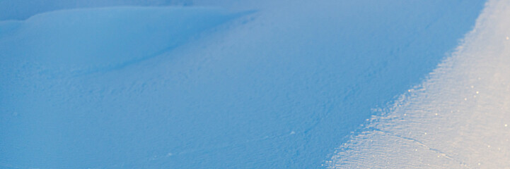 Beautiful winter background with snowy ground. Natural snow texture. Wind sculpted patterns on snow surface. Wide panoramic texture for background and design. Closeup top view with copy space.