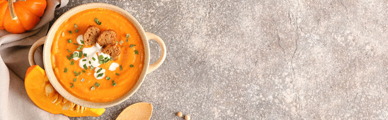 Pot with delicious pumpkin cream soup on grunge background with space for text