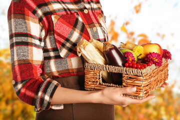 Female farmer holding basket with gathered harvest in autumn garden