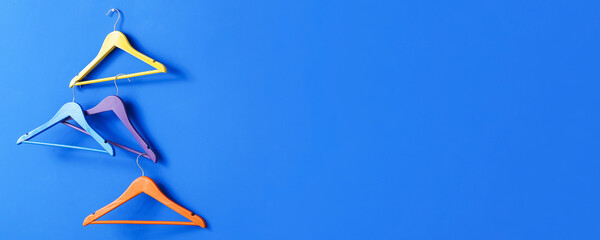 Different clothes hangers on blue background with space for text
