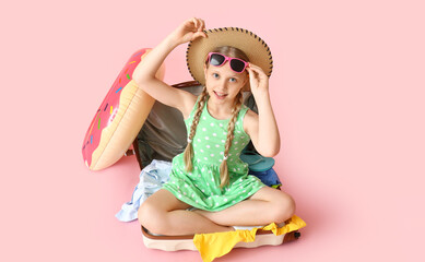 Happy little girl sitting in suitcase on pink background