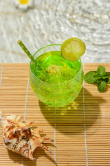 Glass of fresh lime soda on edge of swimming pool
