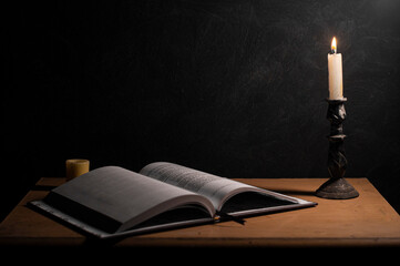 open book being illuminated by a burning candle with a black textured background and strong shadows