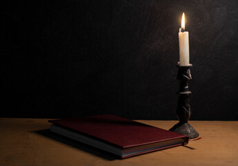 open book being illuminated by a burning candle with a black textured background and strong shadows