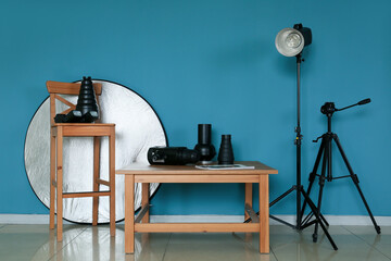 Fototapeta na wymiar Wooden table and chair with different modern equipment near color wall in photo studio interior