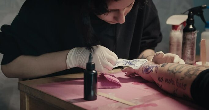 The tattoo artist uses thermal stencil paper to first place a printed design on the skin before applying a tattoo design
