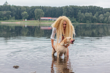 Young beautiful woman with blond curly hair playing with her labrador retriever dog in river.