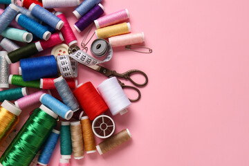Thread spools, scissors, measuring tape and pins on pink background