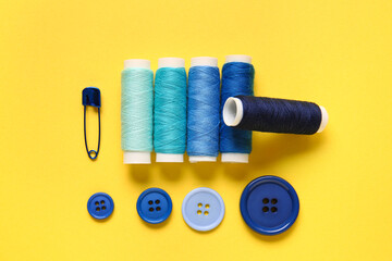 Thread spools, safety pin and buttons on yellow background