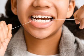 African-American teenage girl flossing teeth on light background, closeup - obrazy, fototapety, plakaty