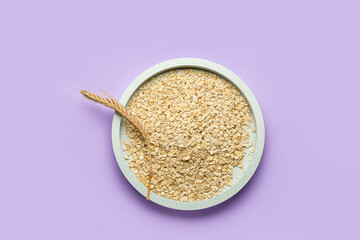 Plate with raw oatmeal and spikelet on lilac background
