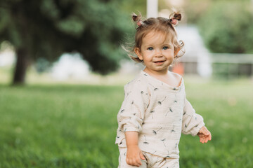 cute little smiling girl with a funny hairstyle hides behind trees and runs and plays in the park