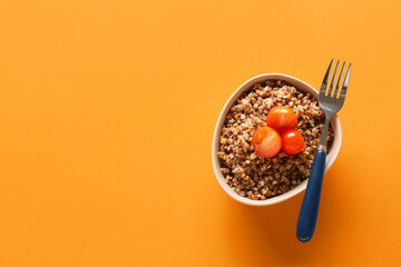 Bowl of tasty buckwheat porridge with tomatoes on orange background