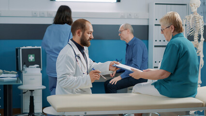 Fototapeta premium Specialist needing signature of patient on consultation files to give health care treatment after doing checkup visit. Elder woman signing examination documents in medical cabinet.