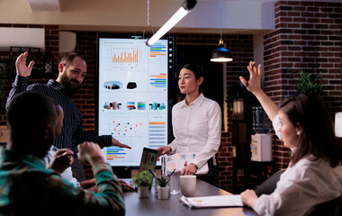 Woman raising hand to ask a question in late night business meeting with sales department in...