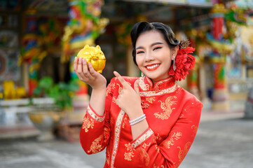 Asian beautiful woman wearing cheongsam with golden piggy bank at shrine on Chinese New Year