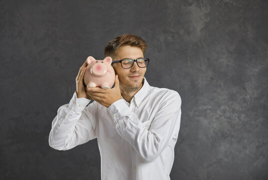 Happy young Caucasian man on black studio background feel excited about money saving in piggybank. Smiling millennial male hold piggy bank make investment for future. Finance stability concept.